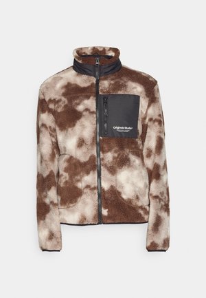 Bruine en crèmekleurige fleecejack met een staande kraag, volle rits en een zwarte ritszak op de borst met het "Originals Studio"-logo.