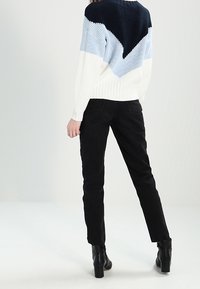 Pletený svetr s vzorem chevron v námořnické modři, světle modré a bílé. V kombinaci s černými slim-fit kalhotami a kotníkovičkami.