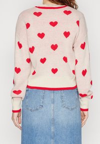 Maglione rosa chiaro con motivi a cuore rossi, collo e polsini a coste rossi in contrasto. Abbinato a una gonna di denim blu con tasche.