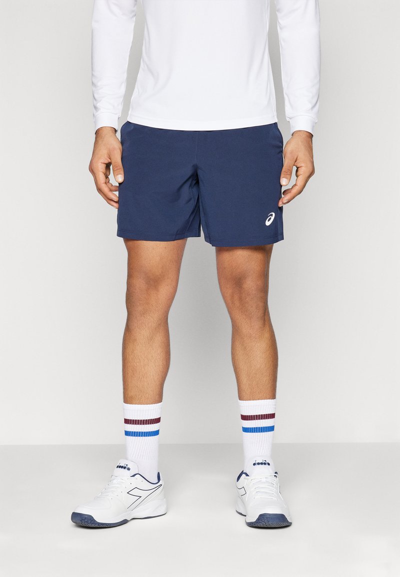 Mørkeblå træningsshorts lavet af letvægtsstof, med en elastisk talje og sidelommer. Sæt med hvide sokker og sko.