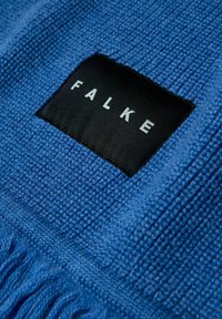 Tissu bleu texturé avec des bords à franges, présentant une étiquette noire affichant le nom de la marque "FALKE" en lettres argentées.