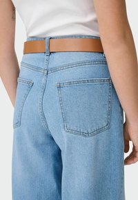 Světle modré džíny z denimu s vysokým pasem, které mají dvě zadní kapsy a hnědý kožený pásek. Látka má hladký, texturovaný povrch.