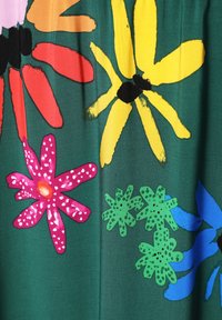 Țesătură verde cu un model floral care include flori roșii, galbene, roz, albastre și verzi, între care accente cu buline și solide.