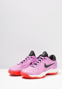 Nike träningsskor med en rosa gradientovandel, svarta detaljer och ett texturerat mönster. Har en vit mellansula och en orange gummisula.