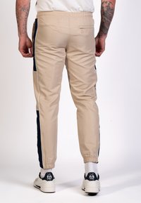 Beige tapschoenen joggers met marineblauwe zijkanten, elastische tailleband, ritszak en opgerolde hems, gemaakt van een gladde, lichte stof.