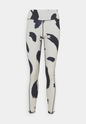 Legginsy z wysokim stanem z czarnymi abstrakcyjnymi wzorami pociągnięć pędzlem na białym tle, z widocznym przeszyciem szwów wzdłuż boków i środka.