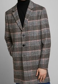 Rutig överrock i grå, svart och rosa toner med rektangulär krage, enkel knappstängning och framfickor. Strukturerad tyg ger djup.