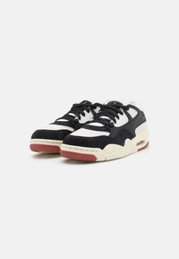Zapatillas en blanco y negro con materiales de ante y cuero, que cuentan con cordones negros, una suela roja texturizada y una unidad de aire visible en la entresuela.
