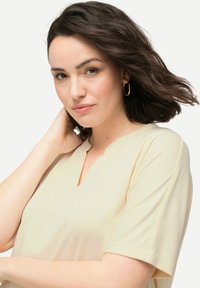 Top a V con maniche corte in un morbido tessuto giallo pallido. Presenta una vestibilità rilassata con una texture liscia e dettagli sottili vicino al collo.