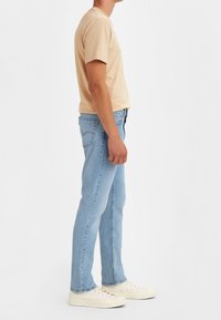 Beige cotton t-shirt paired with light blue denim jeans. The jeans feature traditional five-pocket styling and are straight-fit. Shoes are off-white.