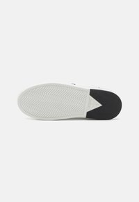 Sola di sneaker bianca con motivo a spina di pesce, con un accento nero sul tallone. Include gomma testurizzata e dettagli di branding sul tallone.