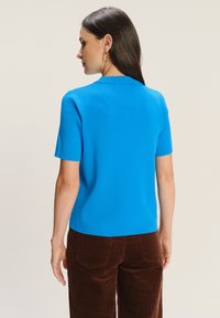 Niebieski t-shirt z krótkim rękawem, wykonany z teksturowanej tkaniny, z okrągłym dekoltem i dopasowanym krojem, w zestawieniu z brązowymi spodniami z kurczaka.