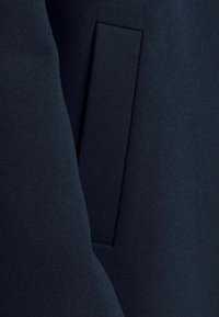 Mörk marinblått tyg med en vertikal sprundficka och en matchande tygflik på en kappa eller jacka.