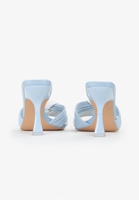 Sandali con tacco alto di color azzurro chiaro, con una finitura lucida, caratterizzati da un design a tracolla intrecciata e una parte posteriore sagomata, poggiati su una suola dai toni neutri.