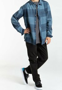 Niebieska koszula w kratę zapinana na guziki, szara koszulka pod spodem, czarne spodnie i czarne sneakersy z niebieskimi akcentami. Długie rękawy i luźny krój.