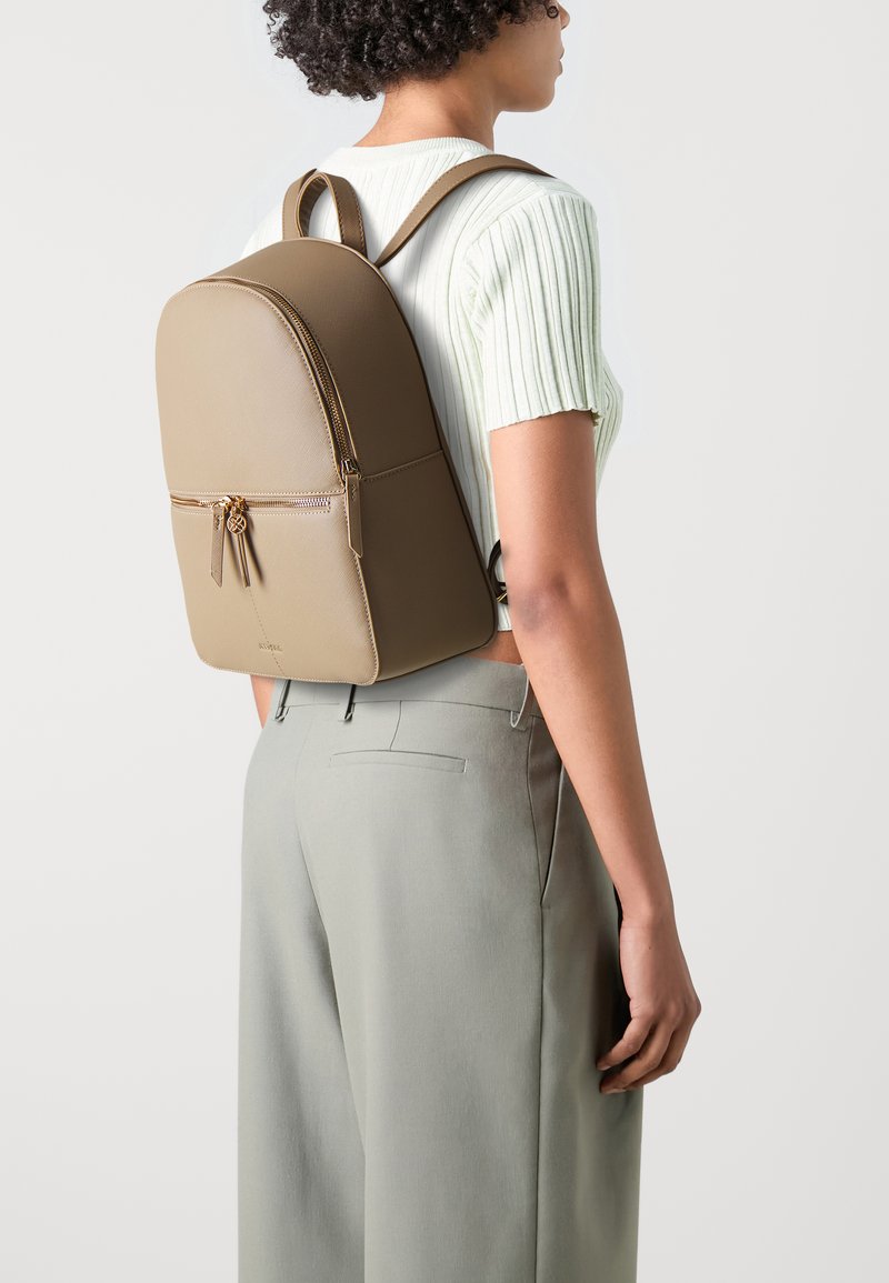 Zaino in pelle sintetica beige con forma arrotondata, accessori in oro, tasca frontale con zip e spallacci regolabili.