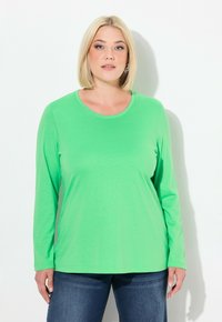 Grünes Langarm-T-Shirt aus weichem, glattem Stoff. Verfügt über einen runden Halsausschnitt und eine lockere Passform, kombiniert mit blauen Jeans.