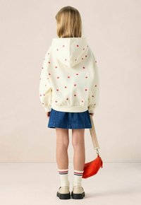 Lichtgele hoodie met rood hartpatroon, denim rok, witte sokken met rode en marineblauwe strepen, en beige schoenen, met een oranje tas.