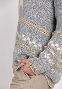 Grau gestrickter Pullover mit einem strukturierten Muster, das leichte rosa Akzente und metallisch gewebte goldene Fäden an den Bündchen und dem Saum aufweist.