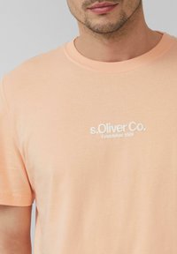 Perzikkleurig katoenen t-shirt met ronde hals, met op de borst een witte geborduurde logo "s.Oliver Co. Established 1969".