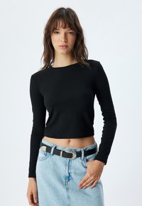 Zwarte langärmige crop top met een ronde halslijn, gecombineerd met een lichtblauwe denim rok en een zwarte riem met een zilveren gespdetail.