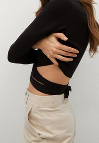 Black ribbed long-sleeve top featuring a cut-out design at the waist, paired with light beige high-waisted pants.