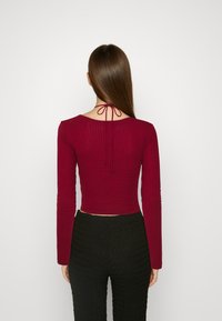 Burgundowy, prążkowany, długi rękaw crop top z wiązanym dekoltem, w połączeniu z czarnymi, teksturowanymi spodniami w wysokim stanie o dopasowanym kroju.