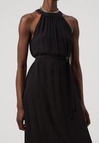 Mustat hienosti muotoillut olkaimeton mekko, jossa on kerätty kaula-aukko, istuva vyötärösolki ja liehuva helma. Sileä pinta ja minimaalinen varusteiden käyttö.