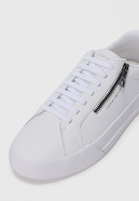 Hvit lær sneakers med flate lisser, sidelukkingdetalj og glatt tekstur. Rund tå og minimalistisk design.