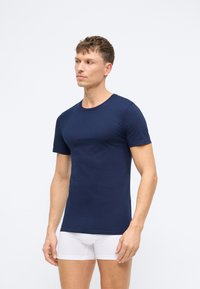 Mørkeblå kortermet T-skjorte laget av bomull, med rund hals og en tettsittende fasong. Brukt med hvite boxershorts.