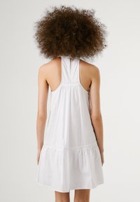 Vestido branco, sem mangas, com costas franzidas, bainha larga e textura suave. Design simples, sem padrões ou detalhes visíveis.