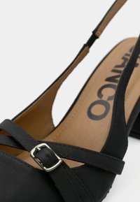 Μαύρο παπούτσι slingback με χαμηλό τετράγωνο τακούνι, με σταυρωτούς ιμάντες και μεταλλικό πόμολο. Ομαλό υλικό και ταμπά εσωτερική επένδυση.