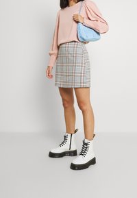 Haut à manches longues rose, jupe mini à carreaux, et bottines blanches à lacets avec une épaisse semelle noire. Sac à main bleu clair avec une texture subtile.