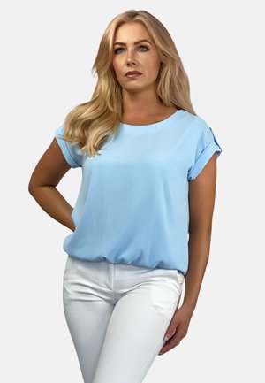 Helles blaues Kurzarmoberteil mit runder Ausschnitt und hochgekrempelten Ärmeln. Kombiniert mit figurbetonten weißen Hosen, die eine entspannte Passform und glatte Textur aufweisen.
