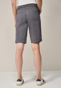 Pantalones cortos grises hechos de una tela ligera con un corte recto, que presentan bolsillos traseros y un dobladillo que llega a mitad del muslo, combinados con zapatillas.