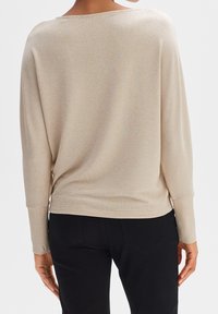 Pull beige surdimensionné à côtes avec manches longues, col large et tissu texturé, associé à un pantalon noir ajusté.
