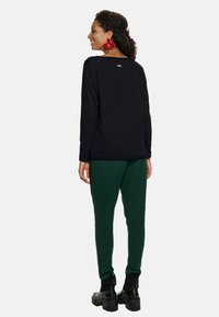 Czarna, długosleeve'owa bluzka o luźnym kroju, w połączeniu z zielonymi, zwężającymi się spodniami. Wyraziste czerwone kwiatowe kolczyki i masywne czarne buty.