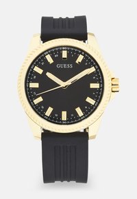 Montre au cadran noir avec marquages horaires ton or, boîtier en métal et bracelet en caoutchouc noir. Dispose d'une lunette tournante et de aiguilles lumineuses pour une meilleure visibilité.