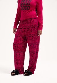 Fukszia hosszú ujjú felső "BEEN SOOO GOOD" felirattal fekete betűkkel, mintás nadrággal kombinálva, amelyen szívek, csillagok és logók szerepelnek ugyanolyan színekben.