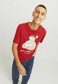 Rød bomulds t-shirt med et grafisk motiv af en tatoveret julemand iført en julestråhat, med denim jeans. Enkel rund halsudskæring, afslappet pasform.