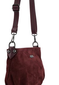 Torebka z zamszu w kolorze burgundowym z teksturowanym paskiem ze skóry, ozdobiona dwoma metalowymi pierścieniami i czarną tabliczką z logo, miękka i lekko luźna w formie.