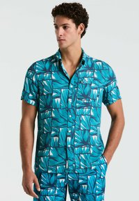 Korte mouwen overhemd in turquoise stof met een geometrisch bladdessin in tinten blauw en wit, met een knoopsluiting en kraag.