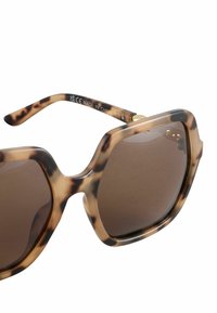 Ochelari de soare cu ramă motive tartaruga, cu lentile mari pătrate, nuanță maro și rame groase. Accente și text aurii pe brațul ochelarilor.