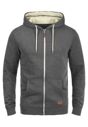 Sudadera con cremallera gris con forro crema, cordones y dos bolsillos frontales. Presenta un pequeño parche de cuero con marca en la parte inferior izquierda.