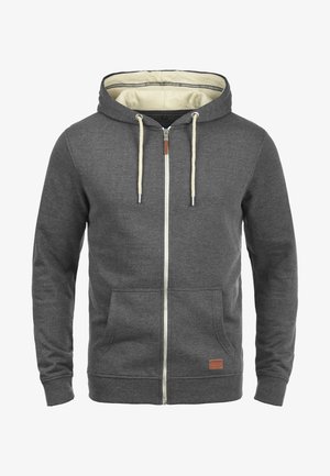 Grå zip-up hættetrøje med cremefarvet foret, snore og to forlommer. Har et lille mærket læderpatch nederst til venstre.