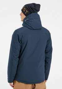 Chaqueta aislante de color azul marino con capucha, que cuenta con un alto cuello y un logotipo bordado en la parte posterior. Material suave y resistente al agua.