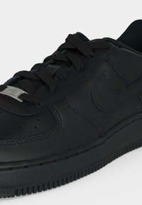 Close-up af sort læder sneakers med sorte snørebånd, stribet tungeetiket og syet swoosh-logo på hvid baggrund.