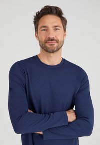 Maglietta a maniche lunghe blu navy realizzata in tessuto morbido, con collo rotondo e maniche aderenti, senza pattern visibili o dettagli aggiuntivi.