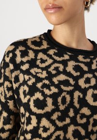 Pull en maille présentant un motif léopard beige et noir, col rond et texture douce. Orné de bords côtelés.