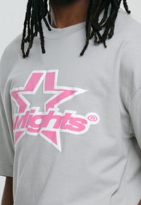 Camiseta gris de algodón con un gran diseño gráfico que presenta una estrella rosa y el texto "wlights". La camiseta tiene un corte relajado y mangas cortas.